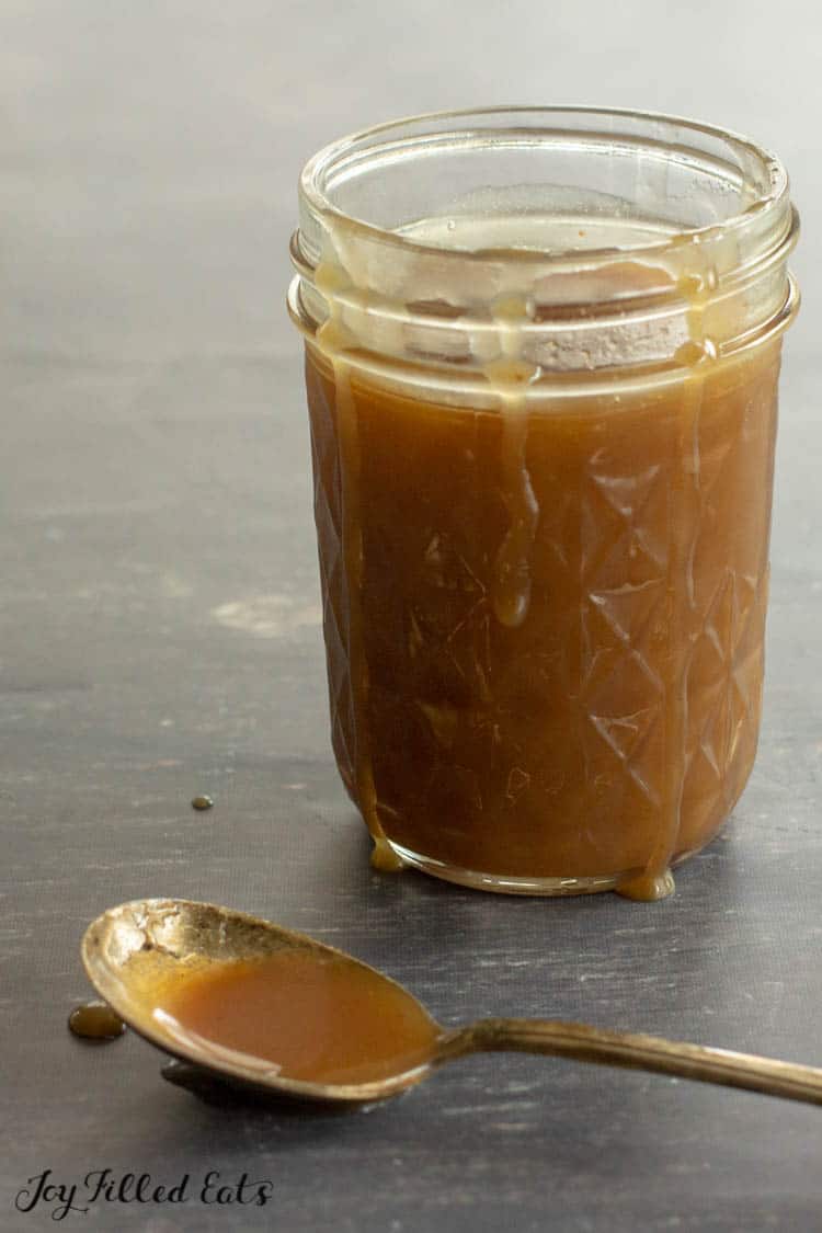 mason jar full of keto caramel sauce with drippings along the side of jar. spoon full of caramel sauce on table