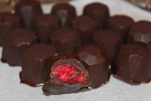 close up on chocolate covered raspberry gems with one gem sliced in half exposing raspberry filling