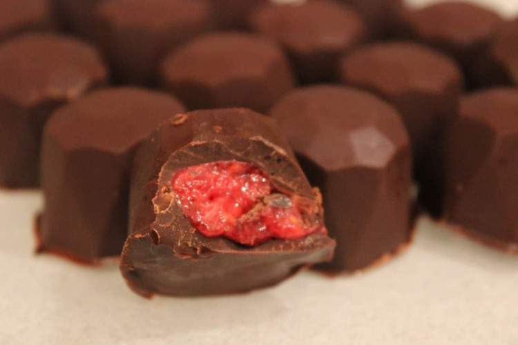 close up on chocolate covered raspberry gems with one gem sliced in half exposing raspberry filling