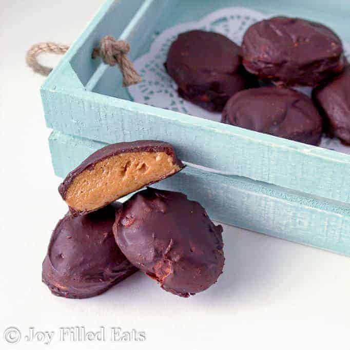 pile of chocolate peanut butter eggs with one egg cut in half placed next to blue wooden box of more chocolate covered peanut butter eggs