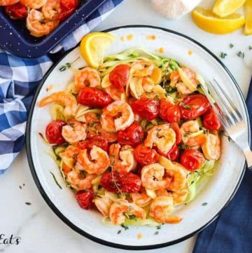baked shrimp with cherry tomatoes in a bowl with a fork resting on the rim set on a table from above