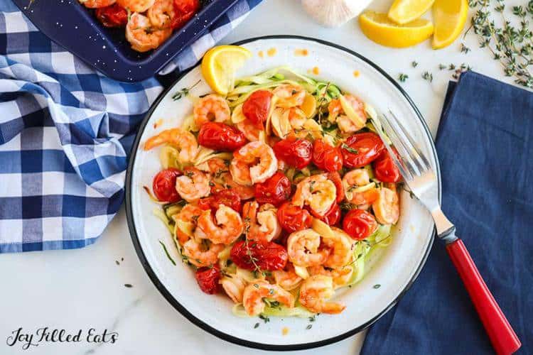 baked shrimp with cherry tomatoes in a bowl with a fork resting on the rim set on a table from above