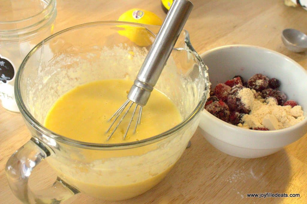 large mixing bowl filled with lemon muffin batter next to small bowl of mixed berries