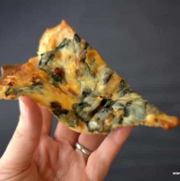hand holding a slice of keto white spinach pizza