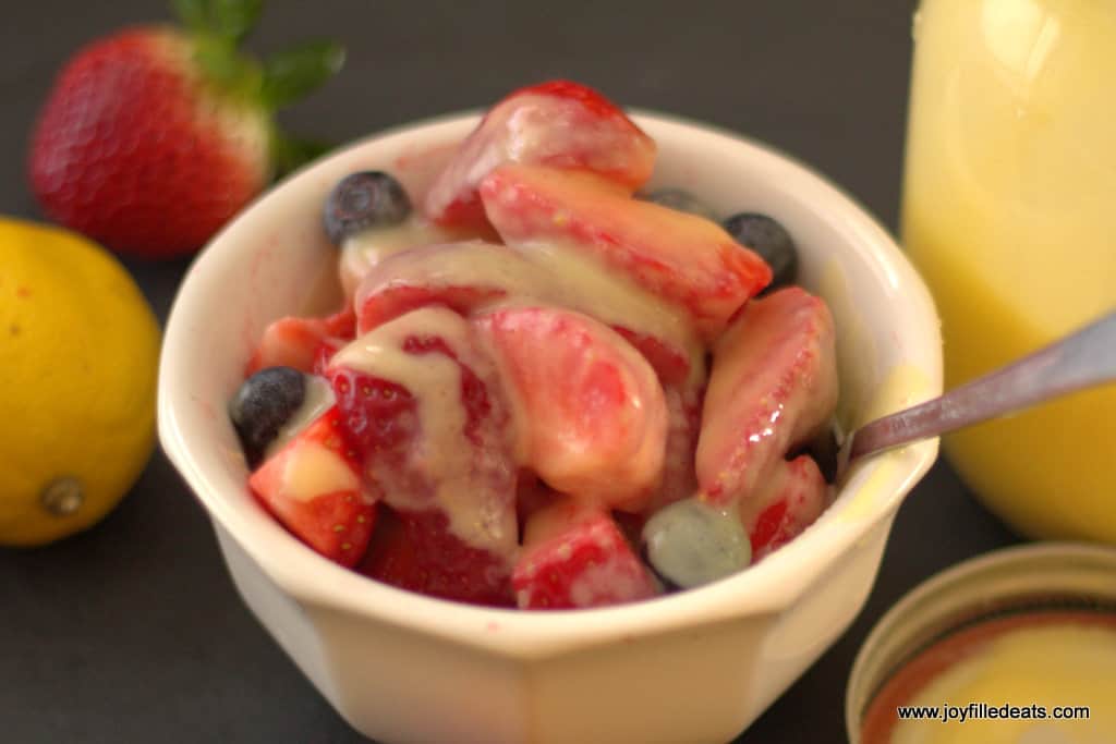 strawberries and blueberries in a white bowl topped with creamy lemon dessert sauce