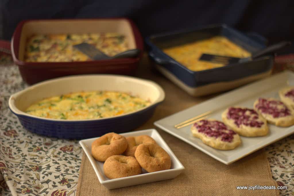 table setting filled with breakfast dishes including three casserole dishes of keto egg bake with cream cheese and donuts and danishes