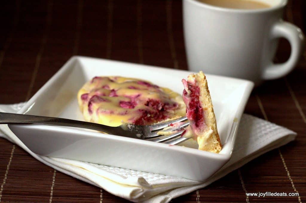 bite of raspberry cream cheese danish on a white resting on a plate with remaining danish set next to a white mug of coffee