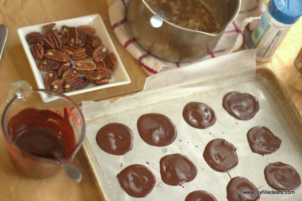 melted chocolate shaped in circles lined on a sheet pan surrounded by ingredients for toasted coconut toffee pecan turtles