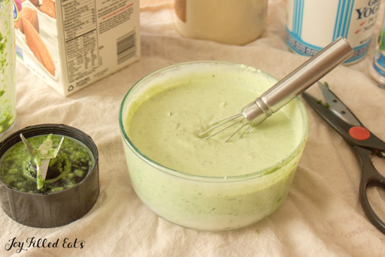 bowl of chive dip with a whisk surrounded by chive dip ingredients and kitchen utensils