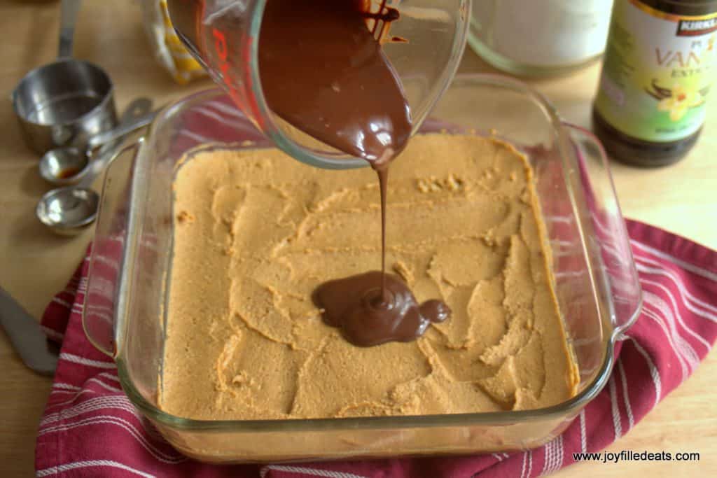 melted chocolate being poured onto peanut butter cookie dough layered in a square baking dish