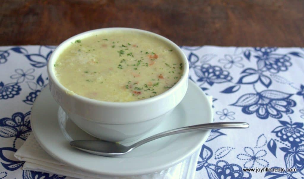 bacon cauliflower soup in a large white bowl set on a white plate with a spoon