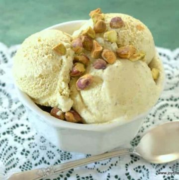 scoops of sugar free pistachio ice cream topped with chopped pistachio nuts in a white bowl next to a spoon