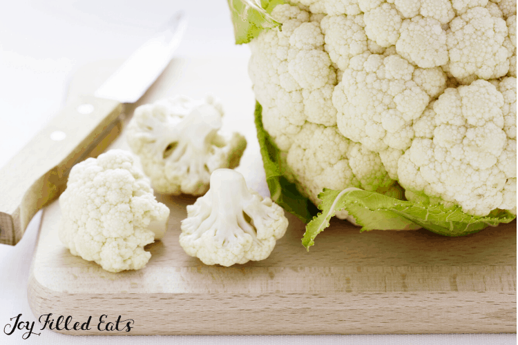 head of cauliflower on cutting board with three florets and a small paring knife with wooden handle
