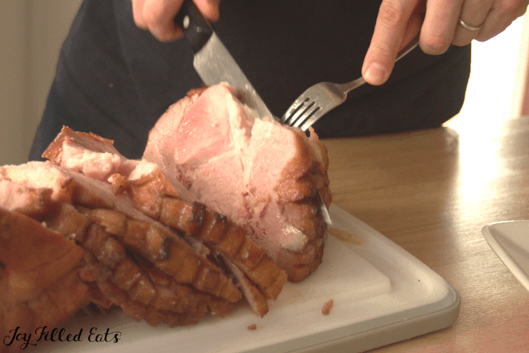person carving maple glazed ham on cutting board