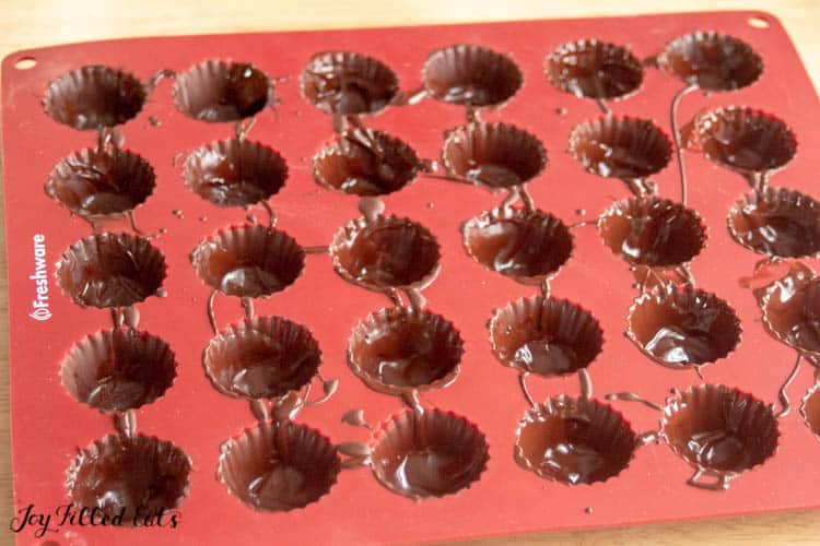 red candy cup mold with chocolate filling in each mold
