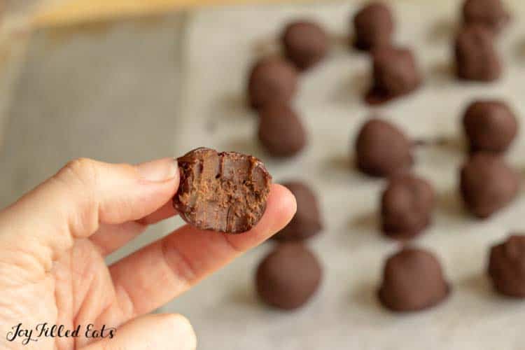 hand holding brownie ball truffle bitten in half in front of truffles arranged in rows on parchment