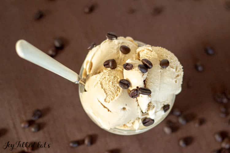 coffee ice cream topped with coffee beans in a bowl with a spoon surrounded by coffee beans on surface