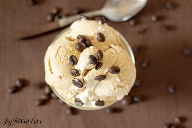 coffee ice cream topped with coffee beans in a bowl surrounded by coffee beans and spoon