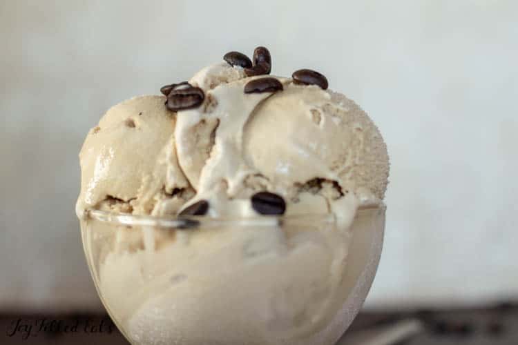 scoops of coffee ice cream in a glass bowl topped with coffee beans close up