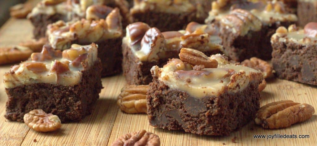 pecan praline brownies arranged on a wooden surface surrounded with scattered pecans