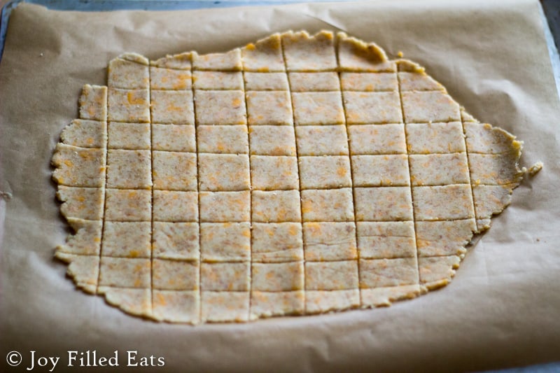 dough for low carb cheddar garlic cheese crisps rolled out onto parchment paper and precut into squares