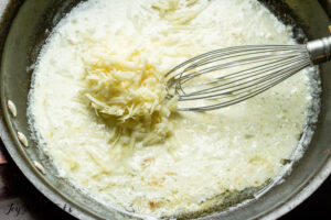 skillet and whisk cooking a cheesy cream sauce