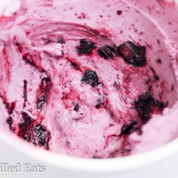 close up of blueberry ripple cheesecake ice cream in a white cup