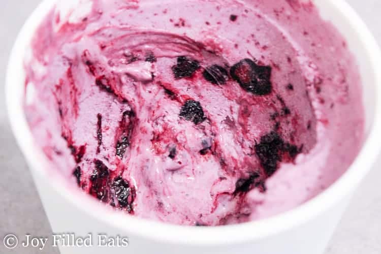 close up of blueberry ripple cheesecake ice cream in a white cup