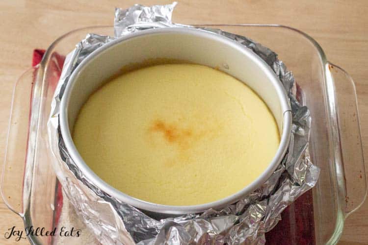 aluminum wrapped cake tin with cheesecake base placed in a small glass casserole dish