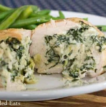 one spinach & artichoke stuffed chicken breast on a white plate sliced in half to show the inside filling