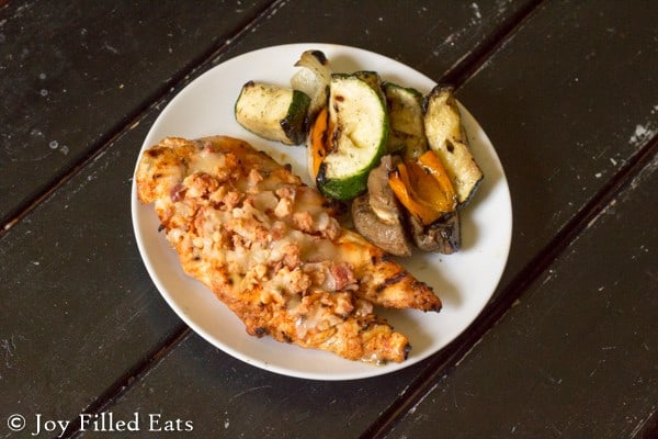 overhead view of grilled cheesy bacon chicken on a white plate served with a side of grilled vegetables