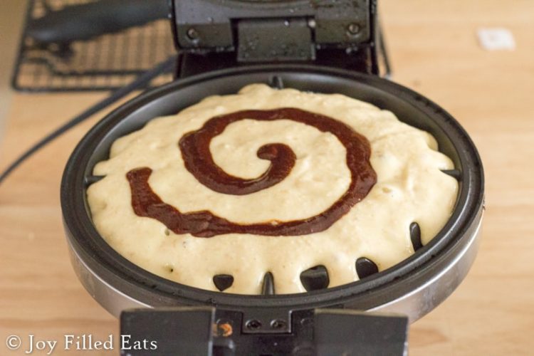 cinnamon roll waffle batter with a cinnamon swirl poured into an open waffle iron