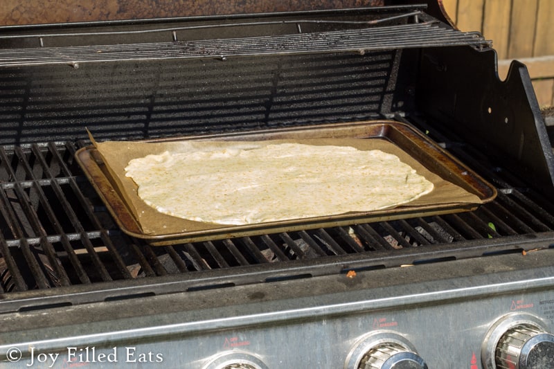 low carb fathead pizza dough rolled onto a sheet pan placed on a grill rack