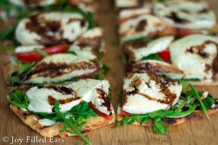 close up on slices of fresh mozzarella & arugula grilled pizza