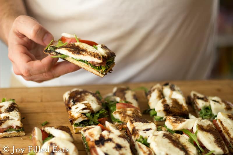 hand lifting slice of fresh mozzarella & arugula grilled pizza from table with more slices