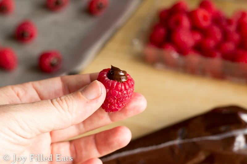 hand holding a raspberry filled with chocolate ganache