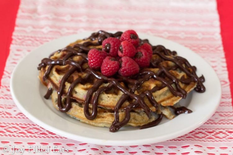 white plate full of chocolate covered raspberry waffles topped with chocolate ganache filled raspberries
