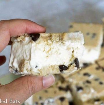hand holding a chocolate chip cookie dough ice cream sandwich with large bite missing