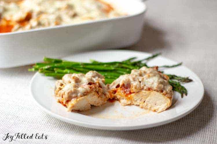 Italian baked chicken with sausage serving cut in half on a plate with green beans set in front of casserole dish