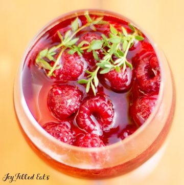 overhead view of a glass of keto sangria filled with raspberries and topped with fresh thyme