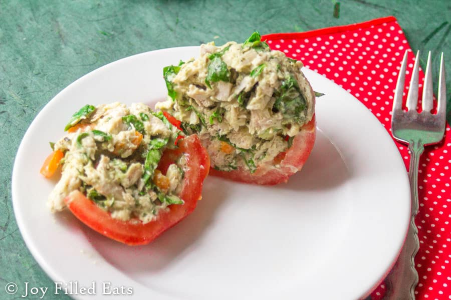 two halves of a tomato cup filled with cilantro lime chicken salad on a white plate