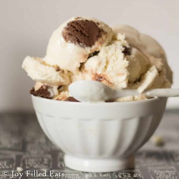 scoops of vanilla ice cream with a chocolate truffle core in a small white bowl with tiny white spoon