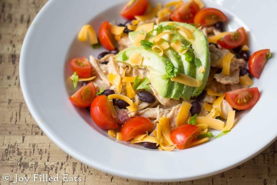 bowl of creamy salsa chicken topped with shredded cheese, sliced cherry tomatoes, black beans and avocado slices from above