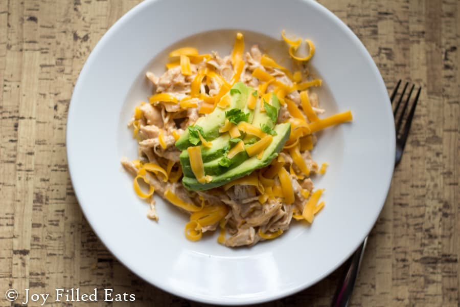 overhead view of creamy salsa chicken in a shallow white bowl topped with shredded cheese and avocado slices set next to a fork