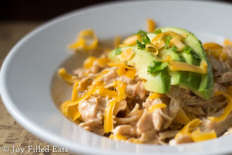 close up of shallow bowl full of Instant Pot Mexican Chicken topped with shredded cheese and sliced avocado