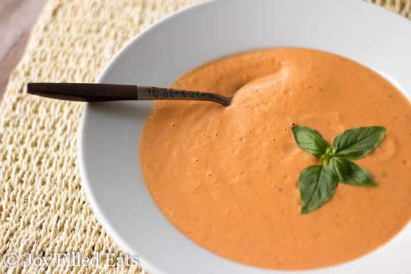 spoon placed inside a white bowl full of fresh tomato and basil soup garnished with fresh basil leaves