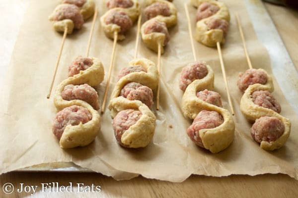 Meatballs skewered with dough arranged on a parchment lined sheet pan before baking
