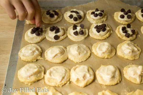 hand sprinkling chocolate chips onto two bite cheese danishes arranged in rows on a parchment lined cookie sheet