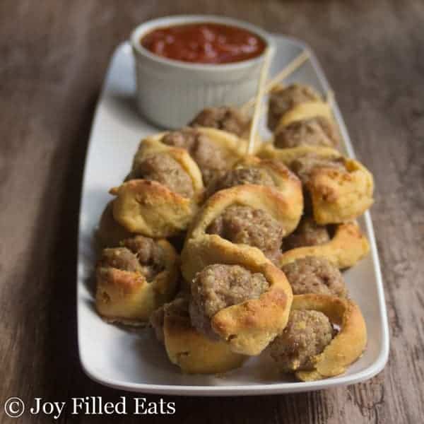 close up on pile of meatball sub kabobs on a white platter with a small dish of marinara sauce