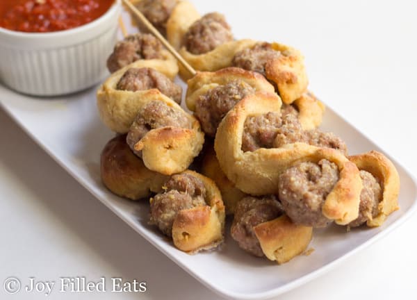 pile of meatball sub kabobs on a white platter with a small dish of marinara sauce